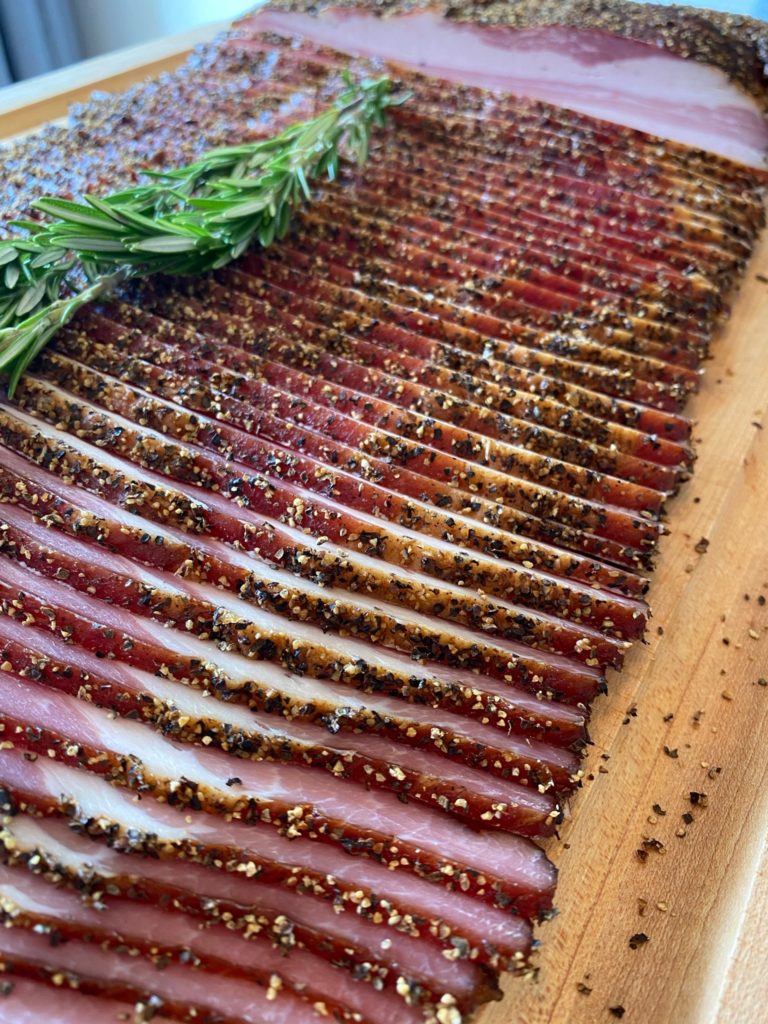 sliced bacon with a sprig of rosemary on a cutting board